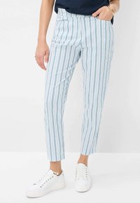Pantalons rayés bleus et blancs avec une coupe slim, dotés de poches latérales et d'une texture lisse, associés à des baskets blanches.