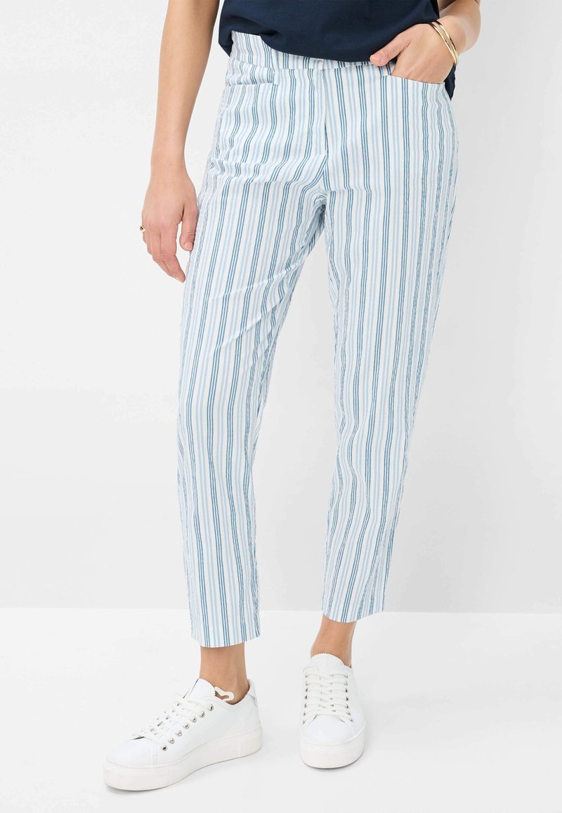 Pantaloni a strisce blu e bianchi con vestibilità slim, dotati di tasche laterali e una texture liscia, abbinati a sneakers bianche.