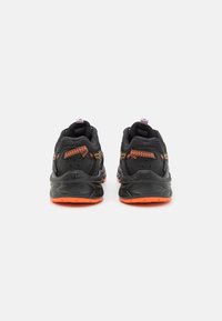 Black athletic shoes with orange soles. Textured upper with mesh lining and a padded collar. Reflective accents and flexible sole design.