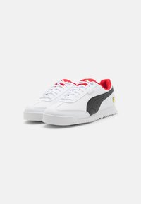 Sneaker bianchi con strisce nere sui lati e dettagli rossi. Realizzati in materiale sintetico liscio, presentano lacci rotondi e una suola testurizzata.