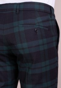 Pantalones de mezcla de lana con un patrón de cuadros en verde oscuro y azul marino, corte ajustado y un bolsillo trasero con un solo botón.