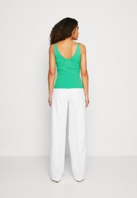 Top de punto verde sin mangas con un diseño en V en la espalda, combinado con pantalones blancos de pierna ancha. La textura suave y la silueta ajustada resaltan la figura.