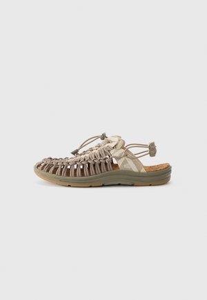 Sandal aperto in marrone chiaro e beige. Presenta una tomaia intrecciata, cinturino regolabile e suola texture con accenti verdi. Inclusa una soletta in sughero.