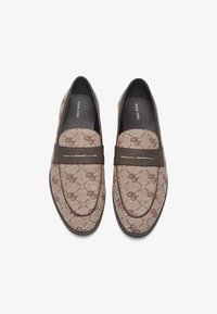 Slipper-Loafer aus beigefarbenem Stoff-Obermaterial mit einem subtilen braunen Muster, brauner Lederband über dem Rist und abgerundetem Zehenbereich.
