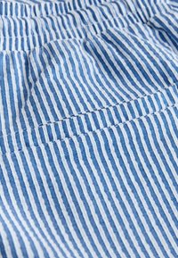 Blue and white striped fabric with a small pocket and visible stitching detail in a close-up view.