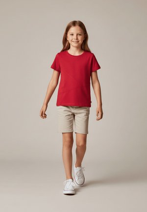 Czerwona koszulka z krótkim rękawem w geometryczny wzór, zestawiona z beżowymi szortami i białymi trampkami, oferująca swobodny, casualowy fason.