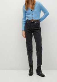 Cardigan court bleu clair avec texture côtelée et boutons noirs, associé à un jean noir taille haute et des bottines noires.