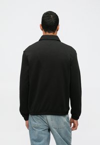 Crna jakna s ovratnikom, rebrastim manžetama i donjim dijelom. Izrađena od glatkog materijala. Uparena s trapericama svijetle boje.