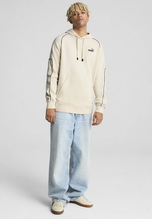 Creme hoodie med sorte accenter, frontlomme og snøre. Båret med lyseblå baggy jeans og beige sneakers. Enkel, afslappet design.