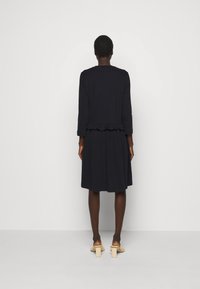 Mörkblå klänning med långa ärmar och volangkant. Tillverkad av mjukt tyg, har en figursydd bodice och en flödande kjol.