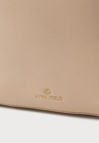 Μπεζ τσάντα χειρός από υλικό με υφή, με χρυσό λογότυπο «ANNA FIELD» στο μπροστινό μέρος. Συμπαγές ορθογώνιο σχήμα με ομαλές άκρες.