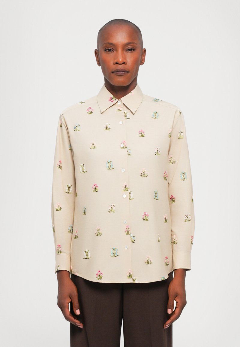 Cămașă butonată de un bej deschis, cu broderie florală în nuanțe de roz și albastru. Prezintă un guler clasic și mâneci lungi. Textura materialului este netedă.