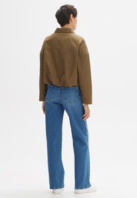 Braune, kurz geschnittene Jacke mit lockerer Passform, kombiniert mit hoch taillierten blauen Jeans. Weiße Sneakers runden das lässige Outfit ab.