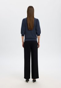 Pullover blu navy con maniche a sbuffo, abbinato a pantaloni neri a gamba larga. Tessuto liscio, vita aderente e design sartoriale.