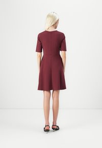 Rochie călcătă până la genunchi, de culoare bordo, cu mâneci scurte, bust ajustat și fustă evazată. Material neted și elastic, cu decolteu la baza gâtului și detalii la cusătura din spate.