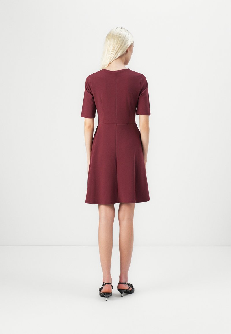 Knielanges kastanienbraunes Kleid mit kurzen Ärmeln, tailliertem Oberteil und ausgestelltem Rock. Glatter, elastischer Stoff mit rundem Ausschnitt und Rückennaht-Detail.