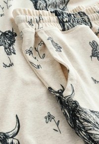 Flødefarvet stof med dyreillustrationer i sort, herunder en giraf og blomster. Elastisk taljebånd og blød tekstur.