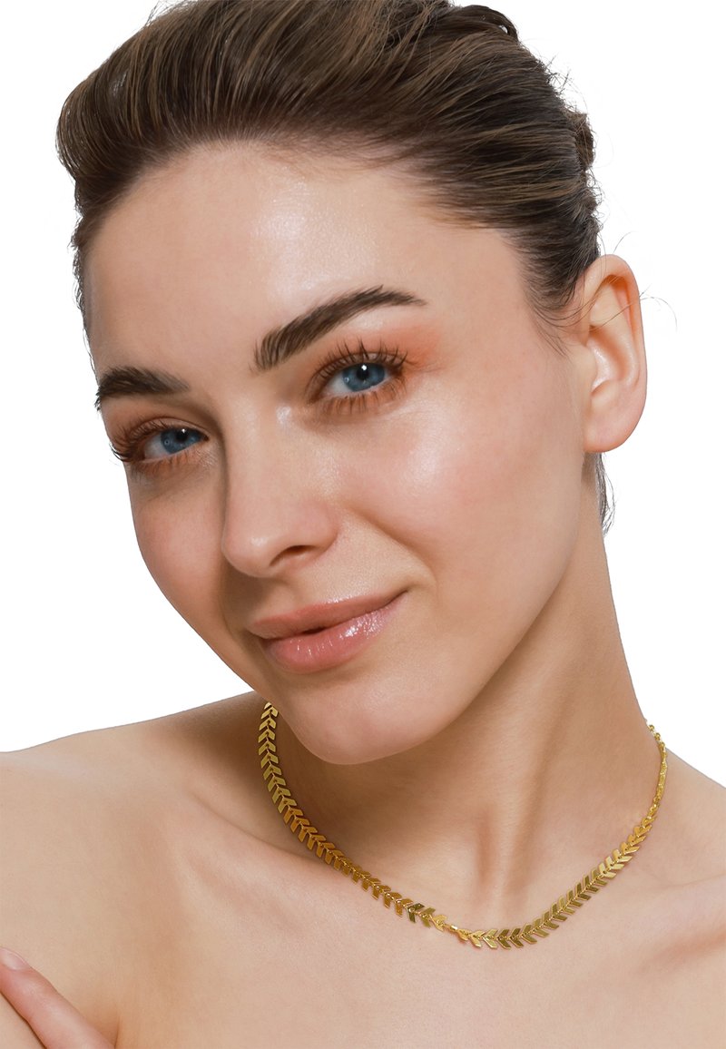 Collier en chaîne dorée avec un motif en chevrons, texture lisse et design flexible, reposant sur la peau nue près de la clavicule.