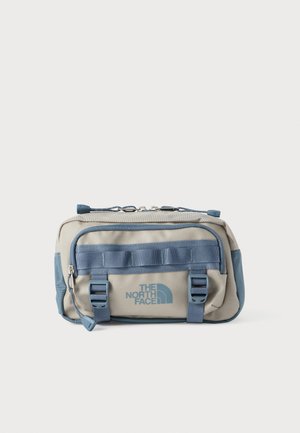 Kompakte beige-blaue North Face Bauchtasche mit Frontreißverschlusstasche, verstellbaren Schnallenriemen und Logo auf der Vorderseite.