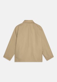 Μπεζ μπουφάν με γιακά, μακριά μανίκια και ελαστικές μανσέτες. Λείο, ελαφρύ ύφασμα με ευθεία γραμμή, χωρίς ορατά κούμπωμα ή σχέδια.