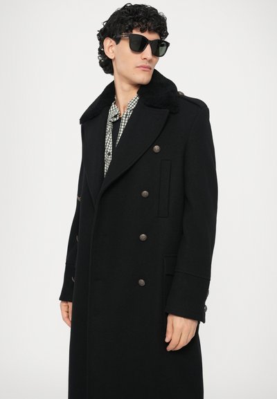 Abrigo de paño negro con cuello amplio y cierre de doble fila. Cuenta con grandes botones, dos bolsillos laterales y una textura suave.