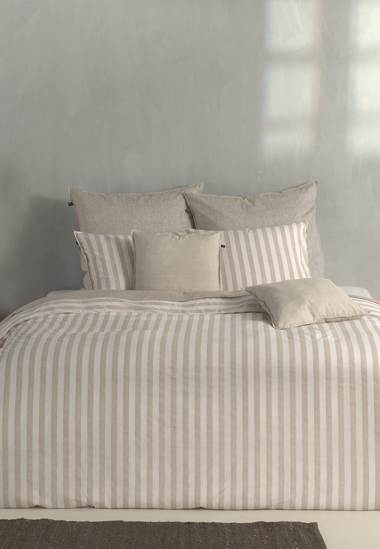 Bettwäsche-Set mit beigem und weißen gestreiften Bettbezug, strukturierten Leinenkissen und verschiedenen Größen von einfarbigen Kissenakzenten.