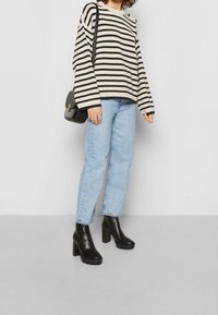 Pull en tricot rayé noir et écru, associé à un jean droit bleu clair et des bottines à talons noires. Comprend un sac à bandoulière.