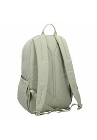 Un sac à dos de taille moyenne en tissu gris clair, doté de bretelles rembourrées, d'une poignée renforcée et d'une finition texturée avec des poches latérales.