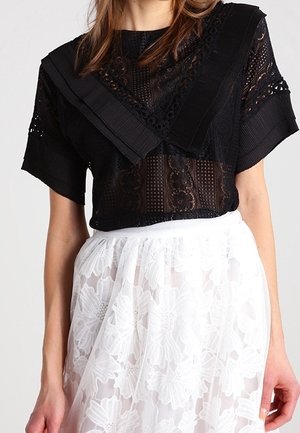 Schwarzes kurzärmeliges Spitzenoberteil mit weitem Kragen, kombiniert mit weißem floralen Spitzenrock, dargestellt von den Schultern bis zur Hüfte.