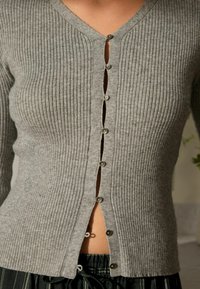 Hellgraue, gerippte Strickjacke mit V-Ausschnitt und Knopfverschluss. Sie hat sieben Knöpfe vorne und einen strukturierten Stoff.
