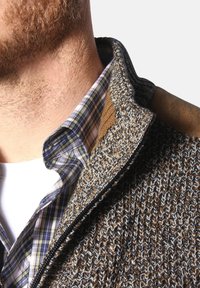 Brauner, strukturierten Strickpullover mit Reißverschluss, der einen braunen Schulterakzent aufweist. Darunter ein kariertes Hemd in Blau, Grün und Weiß.