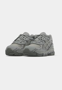 Sive športne copate iz mrežaste in sintetične snovi, vzorčaste prevleke, zaobljen prst in teksturiran podplat za oprijem.