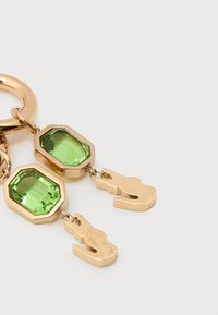 Χρυσό μπρελόκ με δύο μεγάλους πράσινους πολύτιμους λίθους και δύο λεπτομερείς χρυσούς γορίλες σε σχήμα αλιγάτορα σε λευκό φόντο.