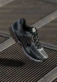 Nike Vomero running shoe in gray and black mesh with rubber accents. Features a cushioned sole, textured side panels, and branded tongue.