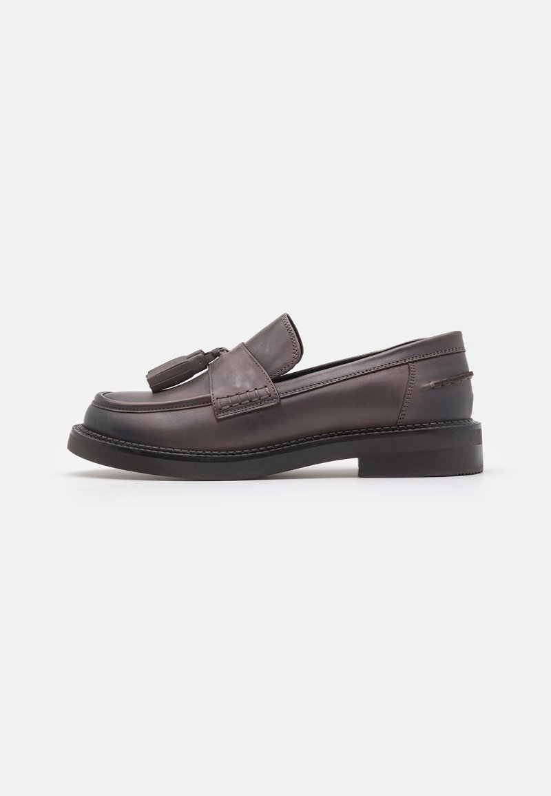 Mocassins en cuir marron avec un accent de pompon, présentant un bout arrondi et une semelle en caoutchouc noire, soulignés par des détails de couture raffinés.