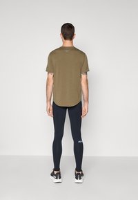 Olive green t-shirt with a rounded hem, paired with fitted navy leggings. Black athletic shoes with white soles and HOKA branding on the legging.