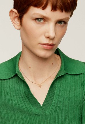 Jersey de punto acanalado verde con cuello en V, acompañado de un delicado collar de oro con pequeños acentos decorativos.