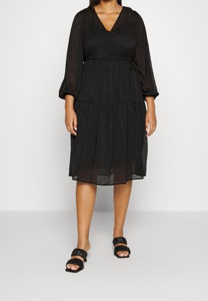 Femme portant une robe midi noire texturée aux manches trois-quarts bouffantes et des sandales noires à bout ouvert avec deux brides rembourrées.