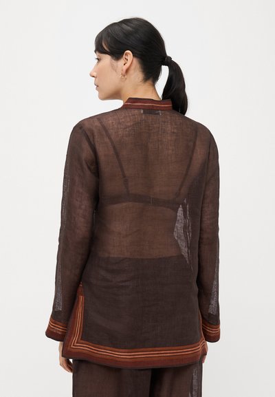 Hnedá priehľadná tunika s dlhými rukávmi, s kontrastným vzorovaným lemom a golierom. Vhodná na vrstvené outfity.