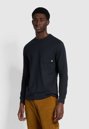 Langärmliges, marineblaues Baumwoll-T-Shirt mit Rundhalsausschnitt, Brusttasche und gerippten Bündchen, kombiniert mit braunen Cordhosen.