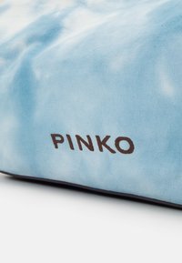Sac en tissu bleu clair avec le mot « PINKO » imprimé en lettres marron foncé près du bord inférieur.