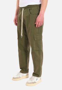 Pantaloni cargo verde oliva con vita elastica, cordino, tasche laterali e tasca applicata sulla coscia. Tessuto di cotone resistente.