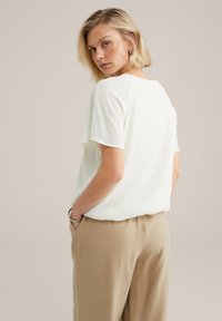 Haut blanc à manches courtes côtelé, col ras du cou, coupe décontractée. Associé à un pantalon beige texturé, avec poches latérales et taille élastique.