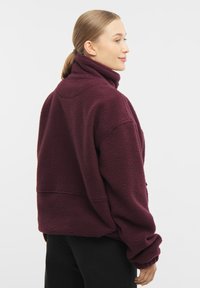 Burgundi színű bolyhos dzseki magas gallérral, ejtett vállakkal és bordázott mandzsettákkal. Puha tapintású, laza, oversize szabású.