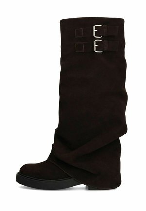 Hoge zwarte suède laars met twee zilveren gespen op de bovenkant en een platte zwarte rubberen zool, tentoongesteld tegen een witte achtergrond.