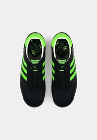 Black athletic sneakers featuring three neon green stripes, textured upper, and a patterned black insole with the Adidas logo.