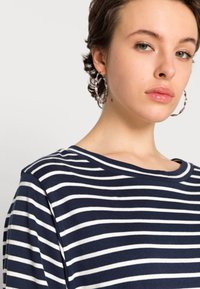 Camisa de gola redonda às riscas azul-marinho e brancas, feita de um tecido suave e com um corte descontraído. Apresenta um padrão de riscas horizontais e um ligeiro elástico.