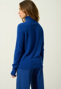 Royal blue golf z wełnianego materiału, dopasowany krój z prążkowanymi mankietami i dołem, w połączeniu z szerokimi spodniami w tym samym kolorze.