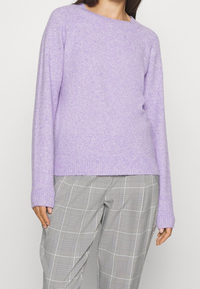 Ljuslila stickad tröja med rund halsringning och ribbade ärmslut, kombinerad med grå och svarta rutiga byxor i lös passform.