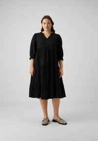 Black tiered dress with puff sleeves and a V-neckline, paired with patterned slip-on shoes featuring a snake print design.
